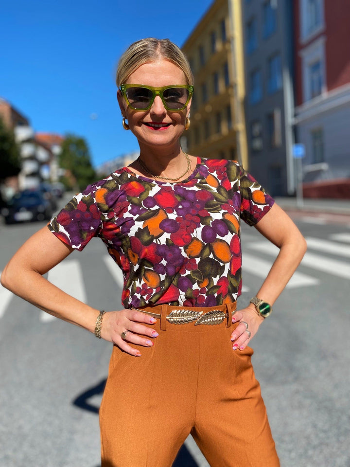 T-skjorte med frukt print fra Dianas Vintage. Hvit bunn med lilla, orange og grønn frukt. Rund hals, korte ermer og kort lengde.