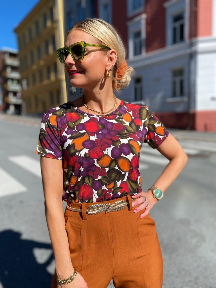 T-skjorte med frukt print fra Dianas Vintage. Hvit bunn med lilla, orange og grønn frukt. Rund hals, korte ermer og kort lengde.