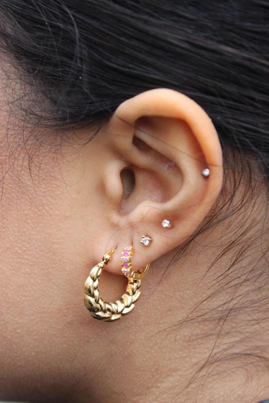 Everly hoops fra merket Pico øreringer i gullbelagt messing metallet er vridd rundt for en lekker effekt. Vist på øret. Foto.